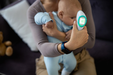 Obraz premium Woman measuring temperature of sick newborn baby at home