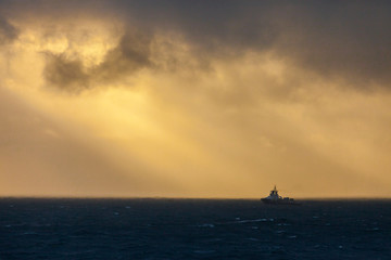 Fototapeta na wymiar An offshore vessel in the ocean with clouds and warm sunlight.