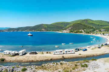 Porto Koufo, Greece, 05/07/2019: View on famous Greek bay with many recreational vehicles parked around the beach and turquoise blue water. Perfect vacation place for camping lifestyle.