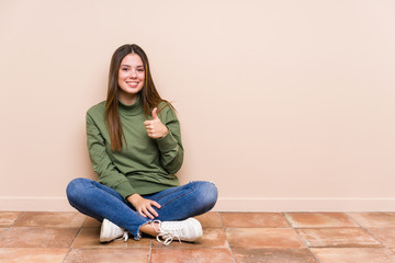 Young caucasian woman sitting on the floor isolated smiling and raising thumb up