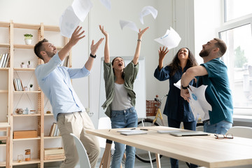 Overjoyed young multiracial business team throwing paper documents in air.