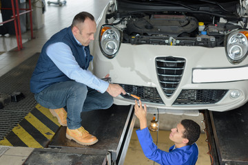 mechanic passing tool to colleague in pit under car