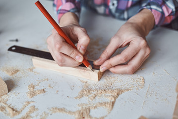 Carpenter hands taking measurement with a pencil of wooden plank. Concept of DIY woodwork and furniture making