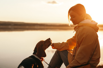 Young woman with dog resting near lake in evening