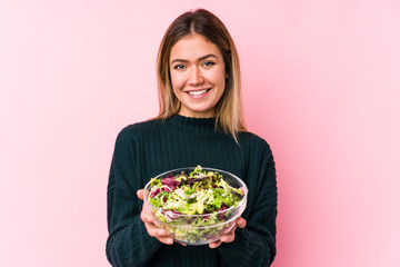 Young caucasian woman holding a salad isolated happy, smiling and cheerful.