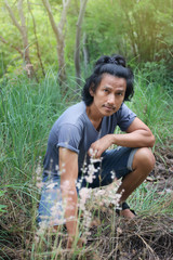 Asian Thai middle aged man long hair in green field on mountain with trees grass element at Thailand. Adult men activity lifestyle with nature forest adventure outdoor. countryside travel concept.