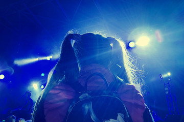 A little girl with two ponytail sits on her father's shoulders at a rock concert in the spotlights,...