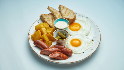 Classic English breakfast: toasts, smoked sausages, fried eggs, potato and fried toasts on a blue plate isolated on grey background