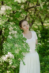 Beautiful girl is walking in the spring park near the trees in bloom. Spring season, sunny weather.