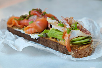 Close up of shot of toasted sandwich with smoked salmon, avocado, shrimp, cream cheese, olive paste and capers. Delicious seafood bruschetta with various ingredients. Top view, copy space, background.