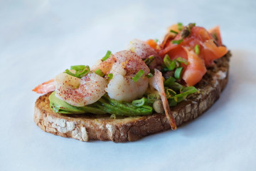 Close up of shot of toasted sandwich with smoked salmon, avocado, shrimp, cream cheese, olive paste and capers. Delicious seafood bruschetta with various ingredients. Top view, copy space, background.
