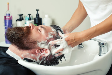 Close-up of brutal caucasian man having his hair washed in hairdressing salon. Barber washing head client. Barber at work.
