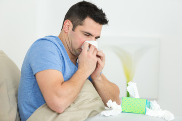 man blowing his nose on the bed