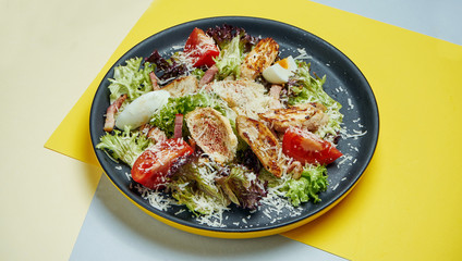 Caesar salad with croutons, parmesan, chicken, egg in black plate on colored background. Restaurant serving. Close up