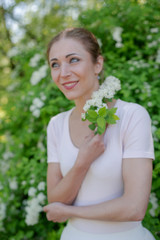 Beautiful girl is walking in the spring park near the trees in bloom. Spring season, sunny weather.