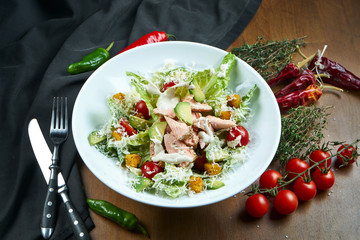 Close up view on served Caesar salad with smoked Salmon in white plate on wooden background. Tasty seafood salad