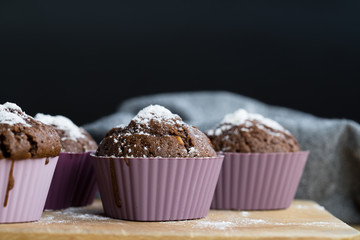 Homemade chocolate cupcakes sprinkled with powdered sugar lying on a wooden board dark background...
