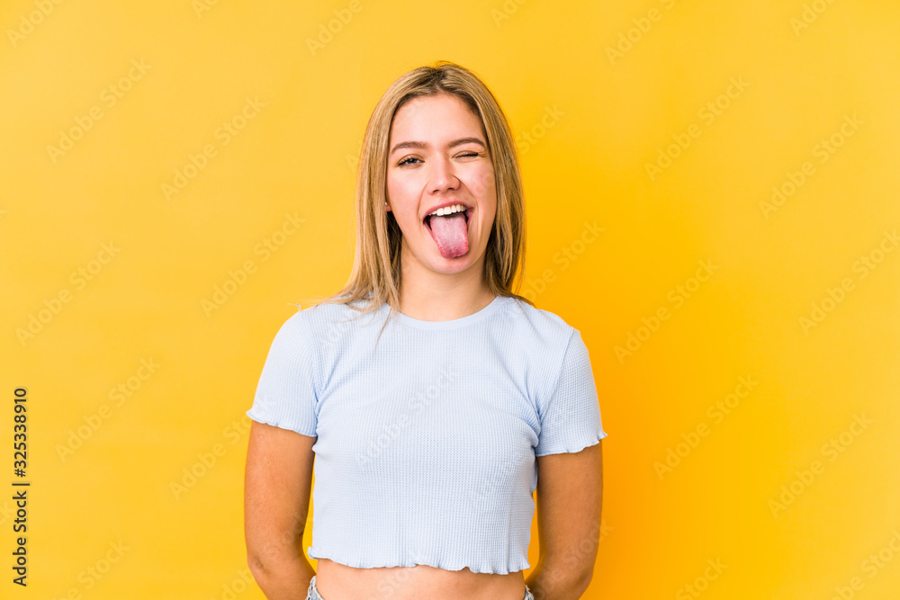 Wall mural Young blonde caucasian woman isolated funny and friendly sticking out tongue.