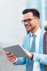 Businessman standing on the street smiling while holding tablet.