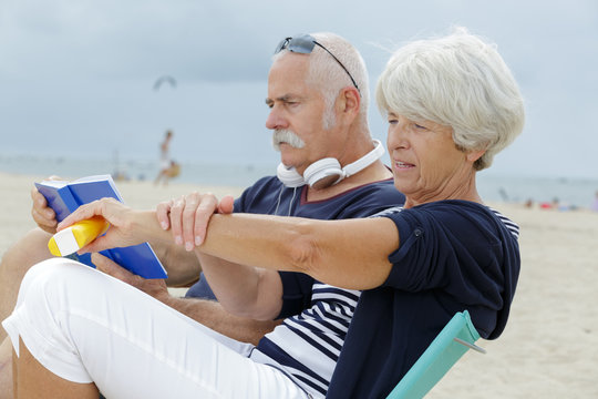 Senior Couple On The Beach Woman Applying Suncream