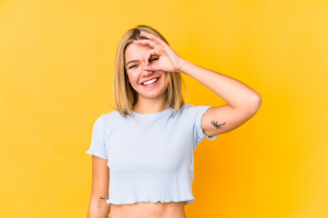 Young blonde caucasian woman isolated on a yellow background excited keeping ok gesture on eye.