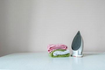 simple scene of the iron and stack of fresh clean colorful towels on the ironing board at home