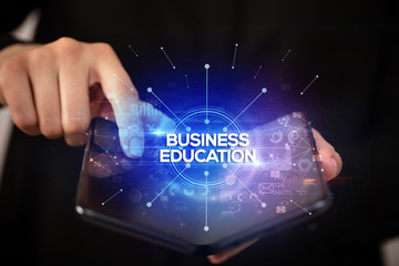 Businessman holding a foldable smartphone with BUSINESS EDUCATION inscription, new business concept