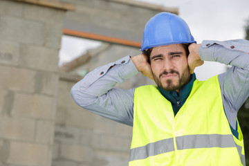 construction worker covering ears to ignore annoying loud noise - obrazy, fototapety, plakaty
