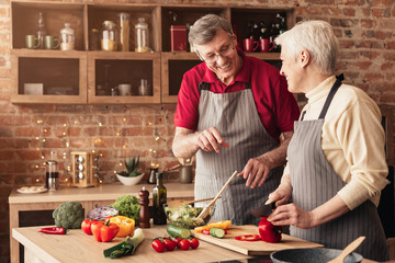 Happy senior couple enjoying preparing dinner together, cooking in kitchen