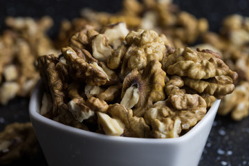 Peeled walnuts lying in a white bowl dark background warm light a healthy snack closeup shot