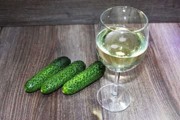 glass of white sparkling wine surrounded by fresh cucumbers on a wooden texture