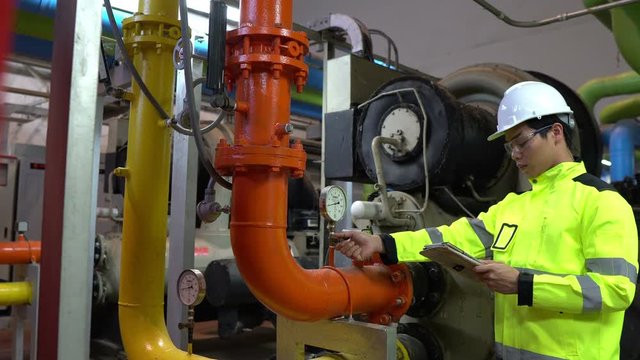 Asian engineer wearing glasses working in the boiler room,maintenance checking technical data of heating system equipment,Thailand people	