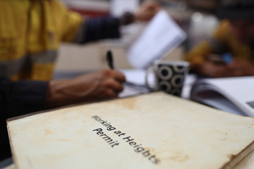 Safe workplace working at heights permit book placing on the table with defocused construction workers writing and organising job hazard analysis risk assessment with teammate prior starting each job 