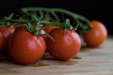 Washed tomatoes lying on a wooden board. Dark background. Close-up view