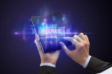 Businessman holding a foldable smartphone with HARDWARE inscription, new technology concept