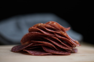 Salami slices lying on a wooden board ready to prepare the dish close-up shot dark background