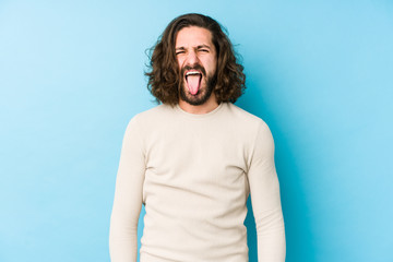 Young long hair man isolated on a blue background funny and friendly sticking out tongue.