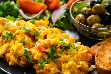 Breakfast - scrambled eggs with vegetables and toasted bread on wooden background