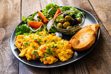 Breakfast - scrambled eggs with vegetables and toasted bread on wooden background