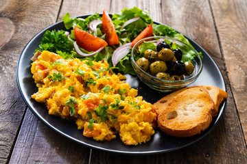 Breakfast - scrambled eggs with vegetables and toasted bread on wooden background