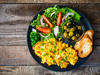 Breakfast - scrambled eggs with vegetables and toasted bread on wooden background