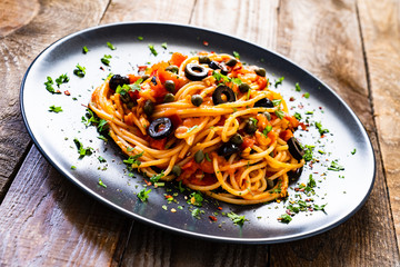Pasta puttanesca with tomato sauce, anchovies, chilli, capers and olives on wooden table