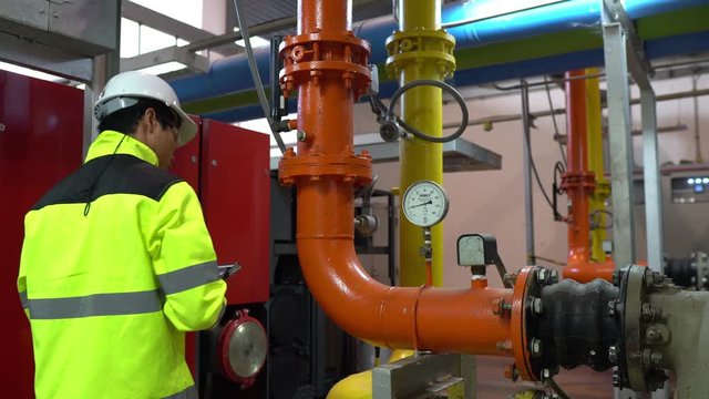 Asian engineer wearing glasses working in the boiler room,maintenance checking technical data of heating system equipment,Thailand people	