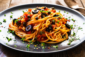 Pasta puttanesca with tomato sauce, anchovies, chilli, capers and olives on wooden table