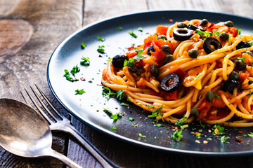 Pasta puttanesca with tomato sauce, anchovies, chilli, capers and olives on wooden table