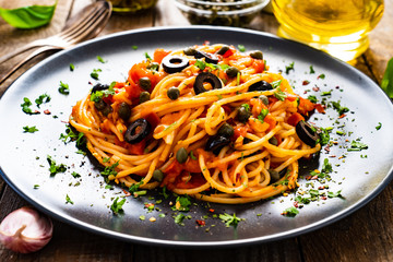 Pasta puttanesca with tomato sauce, anchovies, chilli, capers and olives on wooden table