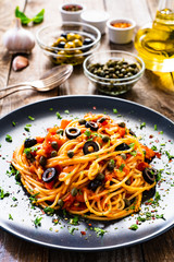 Pasta puttanesca with tomato sauce, anchovies, chilli, capers and olives on wooden table