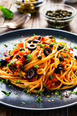 Pasta puttanesca with tomato sauce, anchovies, chilli, capers and olives on wooden table