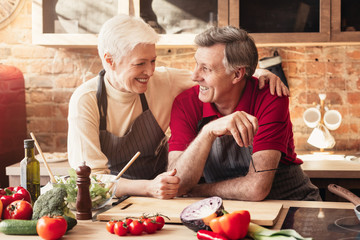 Happy elderly couple embracing in kitchen while cooking dinner together