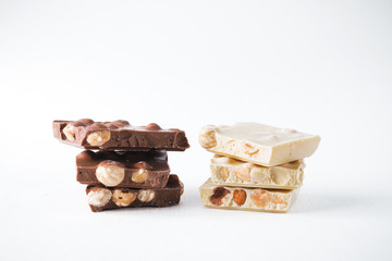 Pieces of dark and white chocolate with nuts in the form of a tower on a white background.